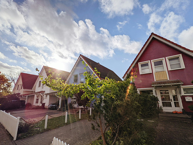 Row of colorful suburban homes along a street under a bright, partly cloudy skyโa familiar setting for deciding whether to rent or buy.